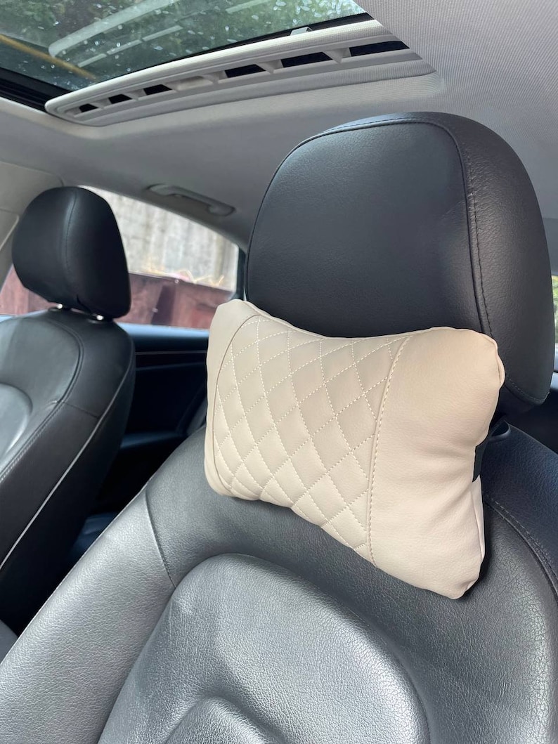May include: Beige quilted headrest pillow for a car seat. The pillow is designed to provide comfort and support for the head and neck.