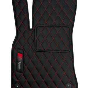 May include: Black car floor mats with red diamond stitching. The mats have a small pocket on the driver's side and a logo on the passenger's side.