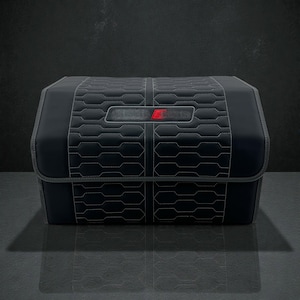 May include: Black, rectangular car trunk organiser with a quilted pattern and white stitching. Features a rectangular emblem with a red accent. The organiser is designed to fit in the boot of a car.