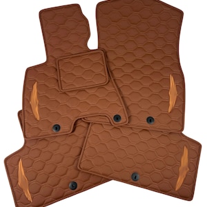 May include: A set of brown car floor mats with a quilted honeycomb design. The mats are shaped to fit a car's interior, with decorative accents and black fasteners. The mats are designed to protect the car's floor.