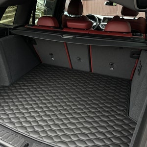 May include: Black leather car trunk mat with a honeycomb pattern. The mat is in the back of a car with red leather seats.