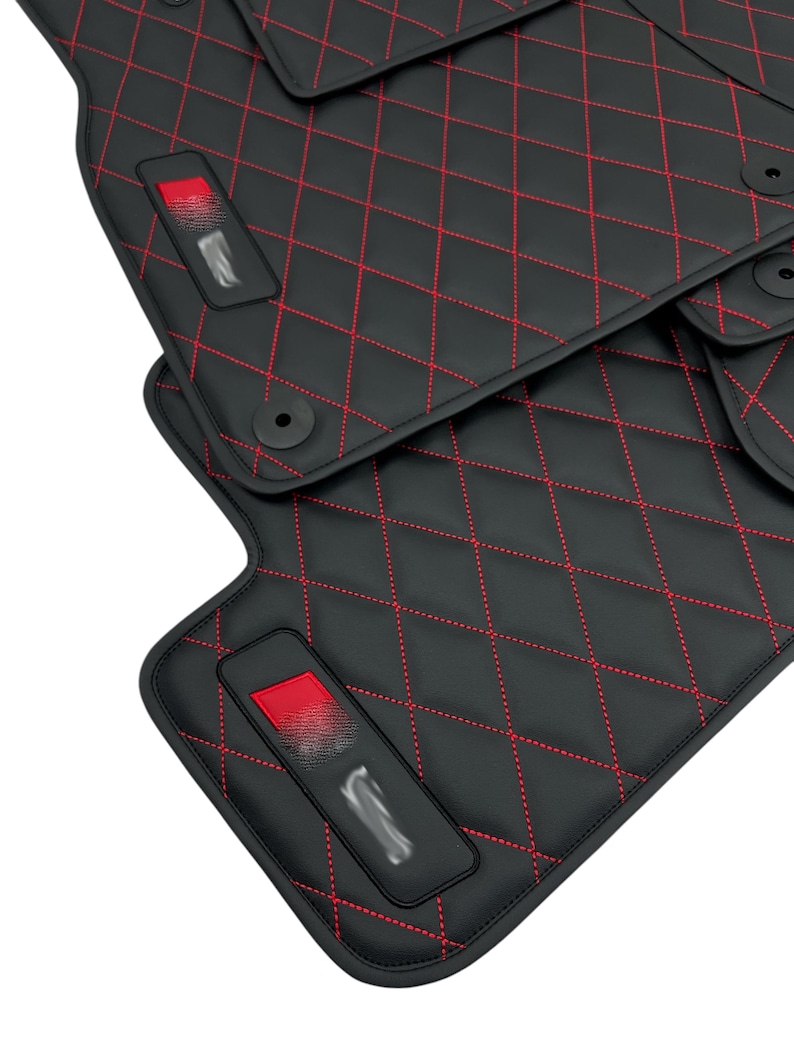 May include: Black car floor mats with red diamond stitching. The mats have a red accent on the driver's side mat.