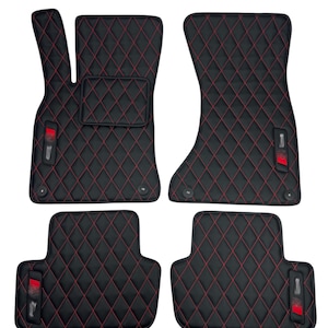 May include: Set of four black car floor mats with red diamond stitching. Each mat has a red logo in the lower corner.