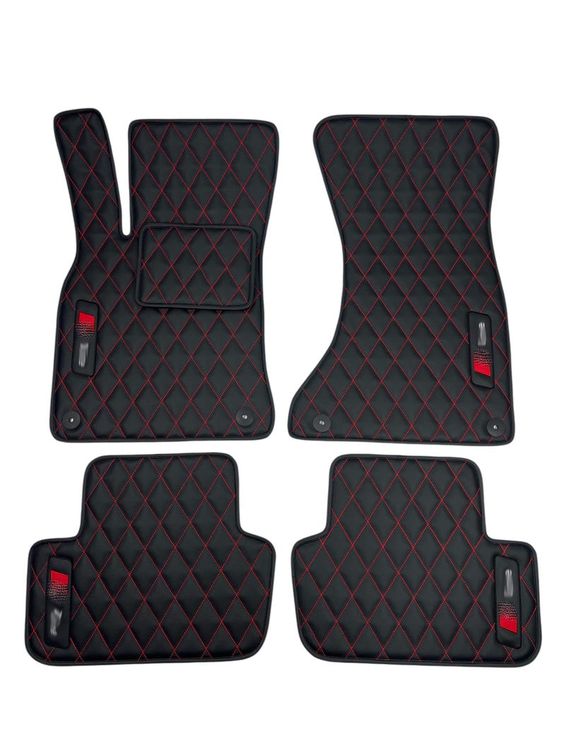 May include: Set of four black car floor mats with red diamond stitching. Each mat has a red logo in the lower corner.