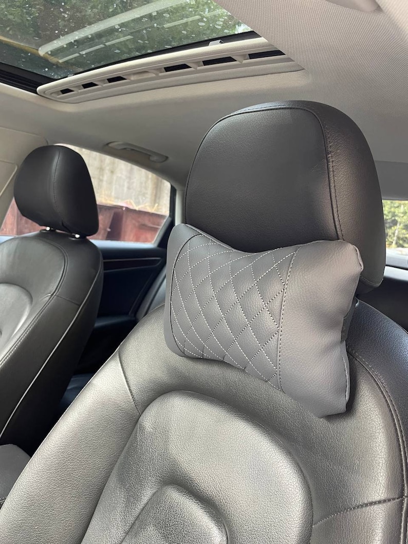 May include: Gray quilted car seat headrest pillow. The pillow is designed to provide comfort and support for the head and neck while driving.