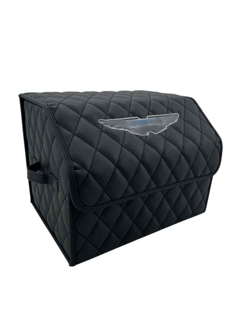 May include: Black quilted car organizer with a diamond pattern. Features a clear emblem on the front. Includes a handle on the side for easy carrying. The organizer is designed to keep items secure and organized.