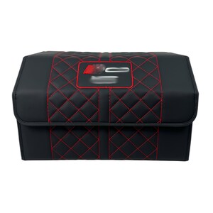May include: Black storage container with red diamond stitching and a red emblem. The container has a rectangular shape with a hinged lid. The stitching creates a quilted pattern on the front and top.