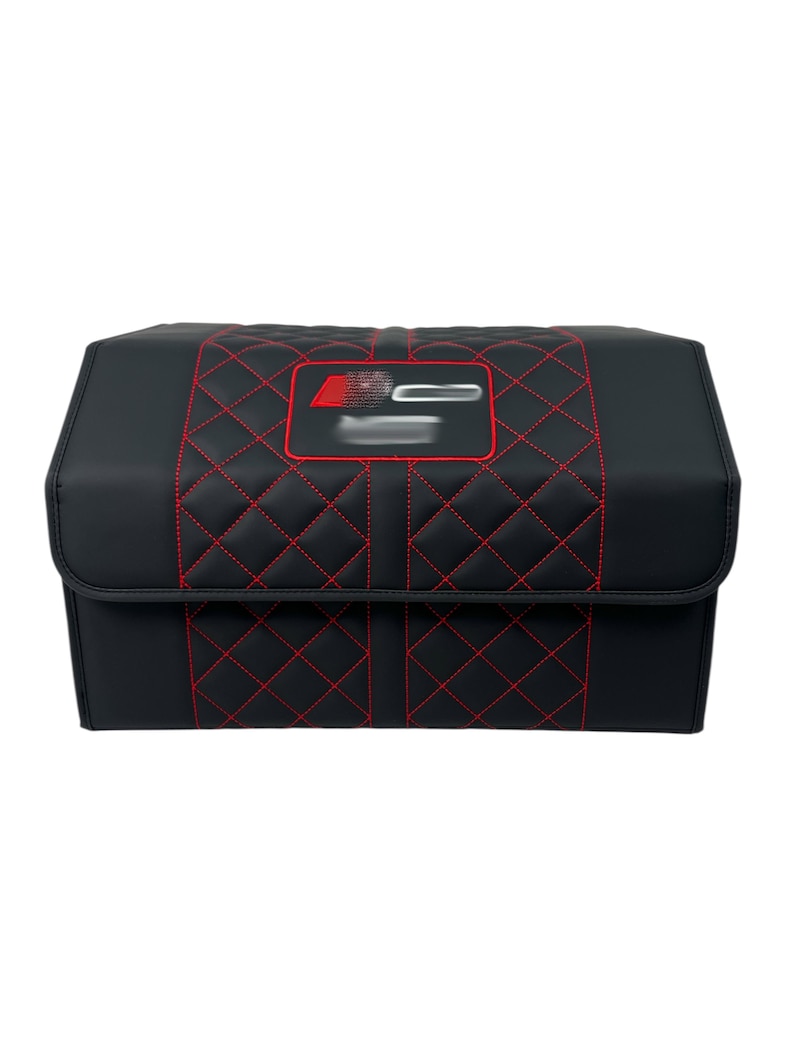 May include: Black storage container with red diamond stitching and a red emblem. The container has a rectangular shape with a hinged lid. The stitching creates a quilted pattern on the front and top.