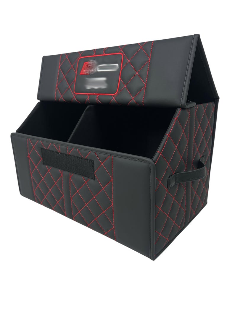 May include: Black car organizer with red diamond stitching. The organizer has a divided interior, a handle, and a lid. The lid features a red-outlined emblem. The organizer is designed to keep a car's interior tidy.