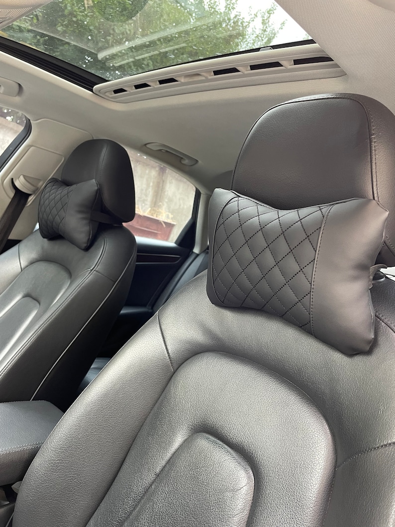 May include: Two black leather car seats with quilted headrests. The headrests have a diamond pattern.