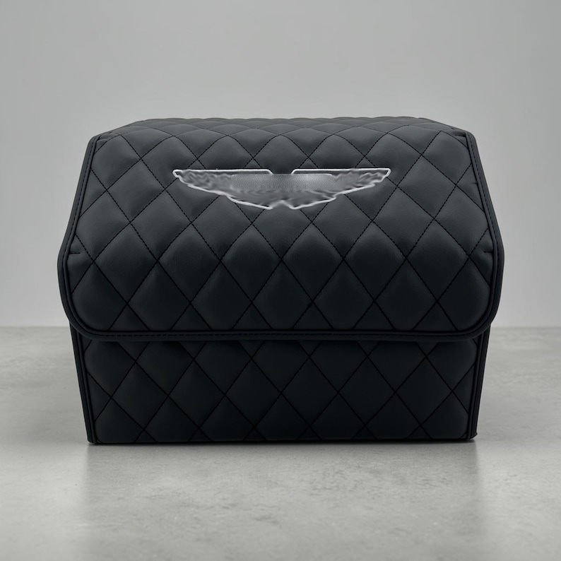 May include: Black quilted storage box with a diamond pattern. The box features a clear emblem on the front. The box is sitting on a gray surface. The box is designed for car storage.