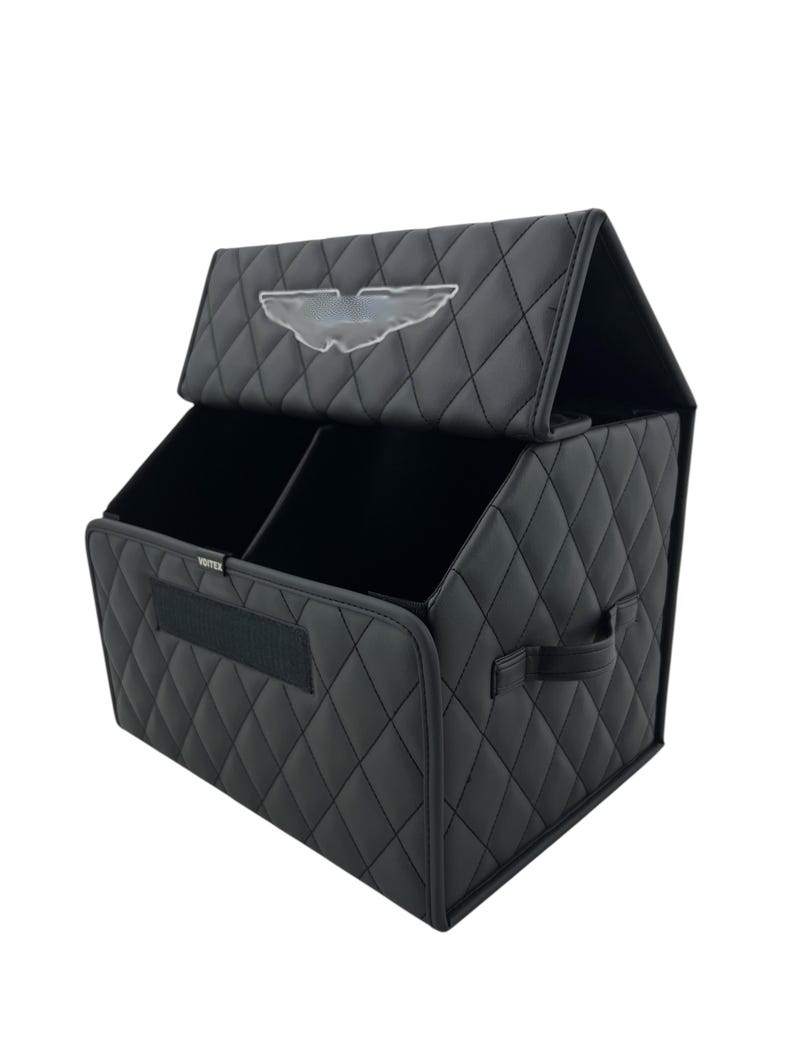 May include: Black car organizer with a quilted pattern and a clear emblem on the lid. The organizer has two compartments and a handle on the side. The word "Vortex" is printed on the front.