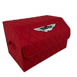 May include: Red quilted storage organizer with a silver emblem on the front. The organizer has a diamond pattern and black stitching. It features a handle on the side for easy carrying.