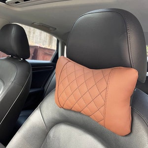 May include: A brown leather car headrest pillow with a diamond pattern. The pillow is designed to provide comfort and support for the head and neck while driving.