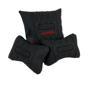 May include: Three black cushions with a geometric pattern and a central oval design. One cushion has a red accent. The cushions are arranged in a stacked configuration, suggesting a seating or support product.