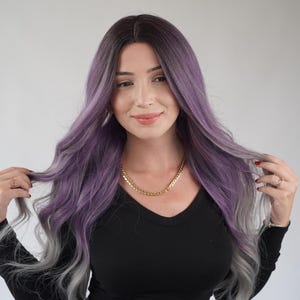 May include: A person with long, wavy, purple and grey hair. They are wearing a black long-sleeved top and a gold chain necklace. The hair has a dark root that fades to a light purple and grey at the ends.