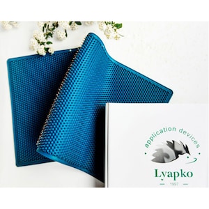 Könnte beinhalten: Eine blaue Akupressurmatte mit einer strukturierten Oberfläche. Die Matte ist in der Hälfte gefaltet und liegt auf einer weißen Oberfläche. Die Matte ist mit "Lyapko application devices - 1997" beschriftet.