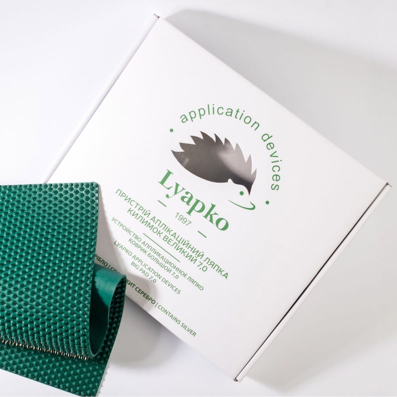 May include: A white box with a green logo that says "Lyapko - 1997 - application devices". The logo features a stylized hedgehog. The box is next to a green, textured, rectangular mat.