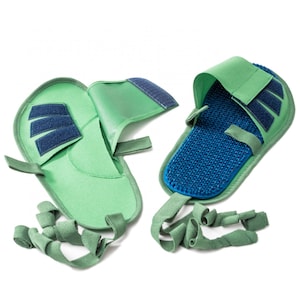 May include: Two green fabric slippers with adjustable straps and blue textured soles. One slipper is folded open to show the inside.