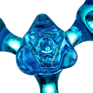 Puede incluir: Primer plano de una escultura de vidrio azul con un diseño triangular en el centro. La escultura tiene una forma única y abstracta.