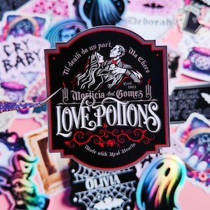 May include: A black and white sticker with a gothic design. It features a couple in a romantic embrace with the text "Til death do us part, Ma Chere" and "Morticia and Gomez 1963". The sticker also says "Love Potions Made with Real Hearts".
