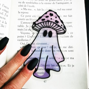 May include: A whimsical sticker featuring a ghost-like figure with a mushroom cap. The mushroom cap is light purple with black spots, and the ghost body fades from light purple to white. The sticker is on a book page.