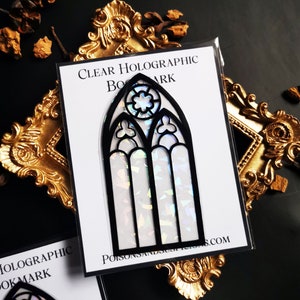 May include: A clear holographic bookmark featuring a black stained glass window design. The bookmark is on a white background with the text "CLEAR HOLOGRAPHIC BOOKMARK" and "POISONSANDSUSPENSIONS.COM".