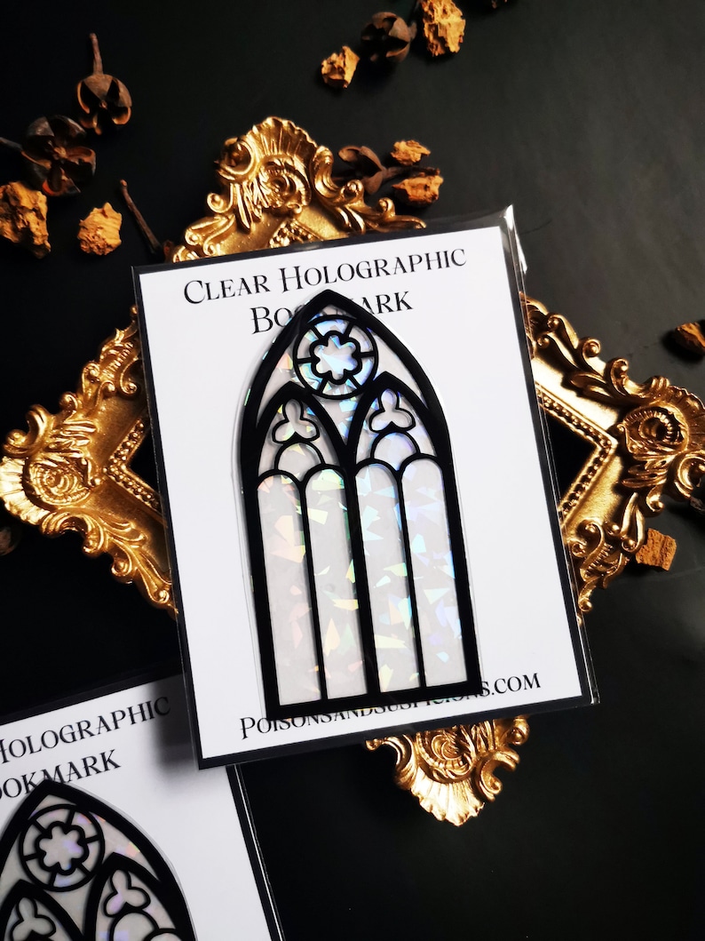 May include: A clear holographic bookmark featuring a black stained glass window design. The bookmark is on a white background with the text "CLEAR HOLOGRAPHIC BOOKMARK" and "POISONSANDSUSPENSIONS.COM".