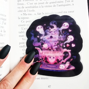 Może przedstawiać: Naklejka przedstawiająca filiżankę do herbaty w kolorze różowym i fioletowym. Filiżanka jest wypełniona piankami i otoczona przez duchy oraz czaszkę. W tle widoczny jest tekst "quest-ce qui me derange den Lindéfinissable".