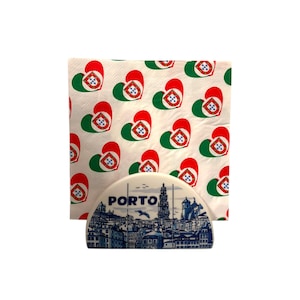 Op de afbeelding: Een witte servethouder met een blauw-witte illustratie van Porto, Portugal, en het woord "PORTO". De servetten hebben een herhalend patroon van rode, groene en witte hartvormen met een wapen.