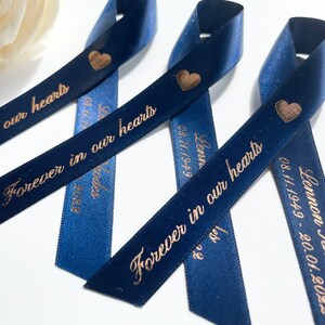 May include: Three navy blue satin ribbons with gold hearts and the text "Forever in our hearts" printed on them. The ribbons are tied together in a knot.