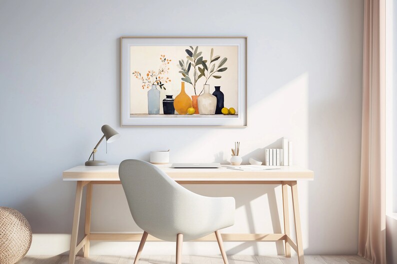 May include: A framed print of a still life featuring a collection of vases with a yellow vase in the center, a leafy branch, and lemons. The print is hanging on a white wall above a desk with a lamp, a laptop, and a chair.