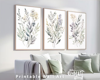 May include: Three framed watercolor prints of botanical arrangements. Each print features a different arrangement of leaves and flowers in shades of green, gray, and purple. The frames are a light wood color. The text "Printable Wall Art" is at the bottom.