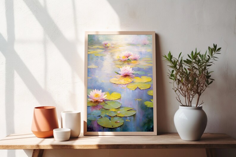 May include: A framed painting of pink water lilies with green lily pads floating on a blue pond. The painting is in a light wood frame and is hanging on a white wall.