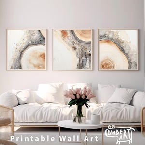 May include: Three abstract watercolor prints with a wood grain pattern in shades of brown, gray, and white. The prints are framed and hung on a white wall above a white couch.