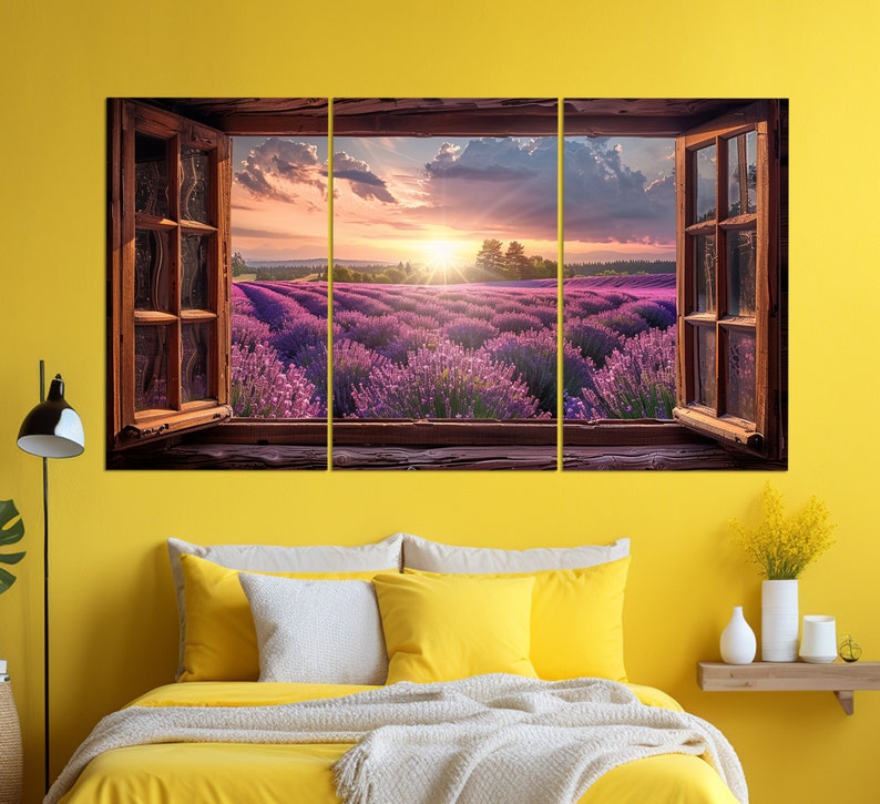 May include: A three-panel canvas print featuring a view of a lavender field through an open window. The field is bathed in the golden light of a setting sun, with a blue sky and fluffy clouds above. The window frame is brown wood, and the window panes are clear glass.