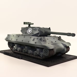 May include: A gray and green model of a military tank with a white star on the side. The tank is on a black base.