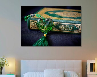May include: A green book with gold lettering and a green heart-shaped charm with Arabic calligraphy. The book is on a dark surface.