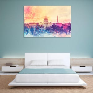 Peut inclure: Impression artistique à l'aquarelle du Capitole des États-Unis et du Washington Monument. L'œuvre présente un style abstrait coloré avec des nuances de rose, de bleu et de jaune. Le tableau est au-dessus d'un lit blanc.