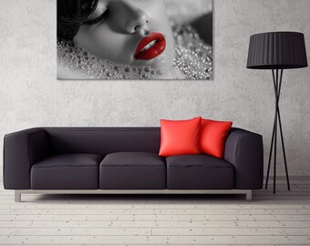May include: A black and white canvas print of a woman with red lipstick in a bubble bath. The print hangs above a black leather sofa with two red pillows. A black floor lamp stands to the right.