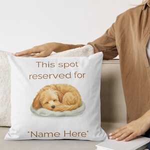 May include: A white square throw pillow featuring a brown illustration of a sleeping puppy curled on a light gray cushion. The text "This spot reserved for" appears above the puppy, and "*Name Here*" is printed in brown below the illustration.