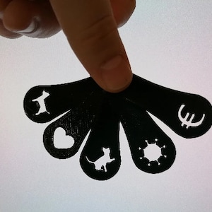 Könnte beinhalten: Schwarzer Plastik-Schlüsselanhänger mit sechs verschiedenen Ausschnitten: eine Katze, ein Herz, eine Katze, eine Sonne, ein Euro-Symbol und eine Katze.