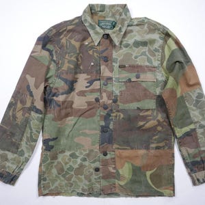 May include: A long-sleeved camouflage shirt with a button-up front and a patch pocket on the left chest. The shirt is made of a cotton blend and has a relaxed fit.