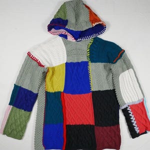 May include: A colorful patchwork hooded sweater with a variety of knit textures and colors, including grey, white, blue, red, green, and yellow.