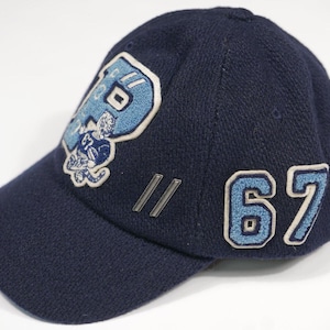 Könnte beinhalten: Marineblaue Baseballkappe mit hellblauem "P"-Logo und einer Footballspieler-Grafik. Die Zahl "67" befindet sich an der Seite. Die Kappe hat einen strukturierten Stoff.