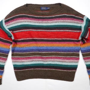 May include: A brown, multi-colored striped sweater with long sleeves and a crew neck. The sweater has stripes of red, orange, yellow, blue, green, and pink.