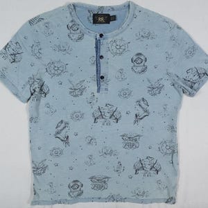 May include: A light blue short-sleeved shirt with a button-up collar and a variety of nautical-themed prints in black. The shirt has a small black tag with the text "RRL" on the front.