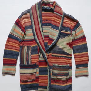 May include: A multi-colored striped cardigan with a shawl collar and two patch pockets. The cardigan is made of a soft, knitted fabric and features a southwestern-inspired pattern. The label on the cardigan reads "Polo Ralph Lauren".
