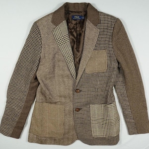 Puede incluir: Una chaqueta de traje marrón, negra y blanca con un bolsillo de parche en el lado izquierdo y un cierre de botón. La chaqueta tiene un patrón de espiga en las mangas y un patrón de cuadros en el lado derecho del pecho.