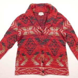 Op de afbeelding: Rode, bruine en witte gepatroneerde cardigan met een shawlkraag en knoopsluiting. De cardigan heeft een geometrisch ontwerp.